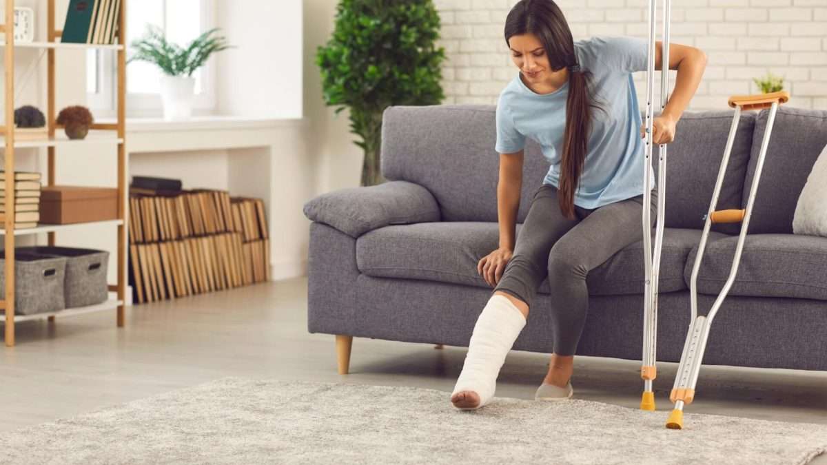 Frau mit einem Gipsverband am Bein, die auf einem Sofa sitzt und Krücken benutzt.
