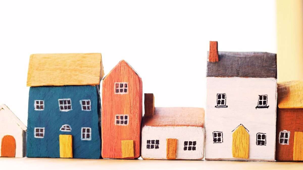 Reihe von bunten Holzhausmodellen in verschiedenen Farben und Formen auf einem weißen Hintergrund.