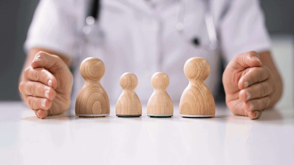 Vier Holzfiguren in abnehmender Größe, gehalten von einer Person mit medizinischer Kleidung.