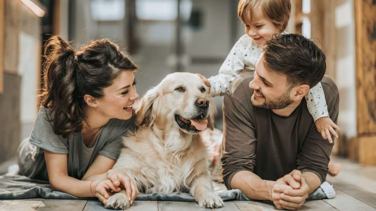 Eine Familie mit einem Golden Retriever, die auf dem Boden liegt und miteinander interagiert.